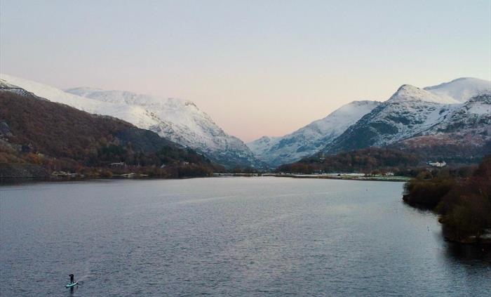 Picture of a lone paddleboarder on a welsh lake with snowy mountains in the background